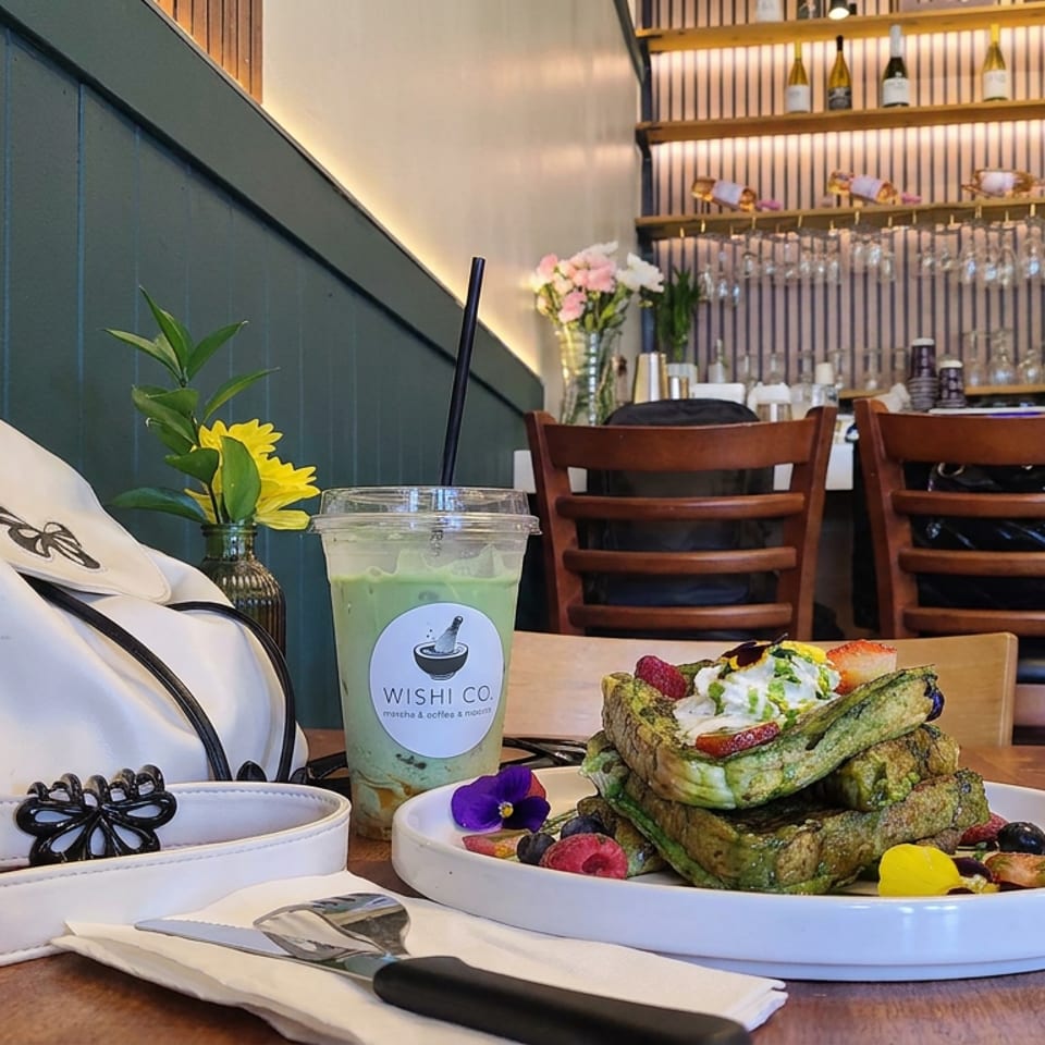 Stack of green waffles topped with cream and berries beside a Wish Co. drink in a warmly lit restaurant.